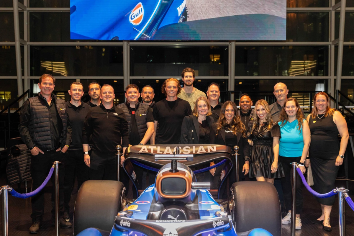 青と黒のレースカーを中心に、多くの人々が笑顔でポーズをとっている集合写真