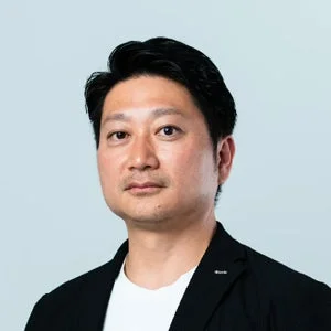 白いTシャツの上に黒いジャケットを羽織ったアジア人男性のポートレート。真顔でカメラを見つめており、ビジネスシーンに適した真面目な印象を与えます。